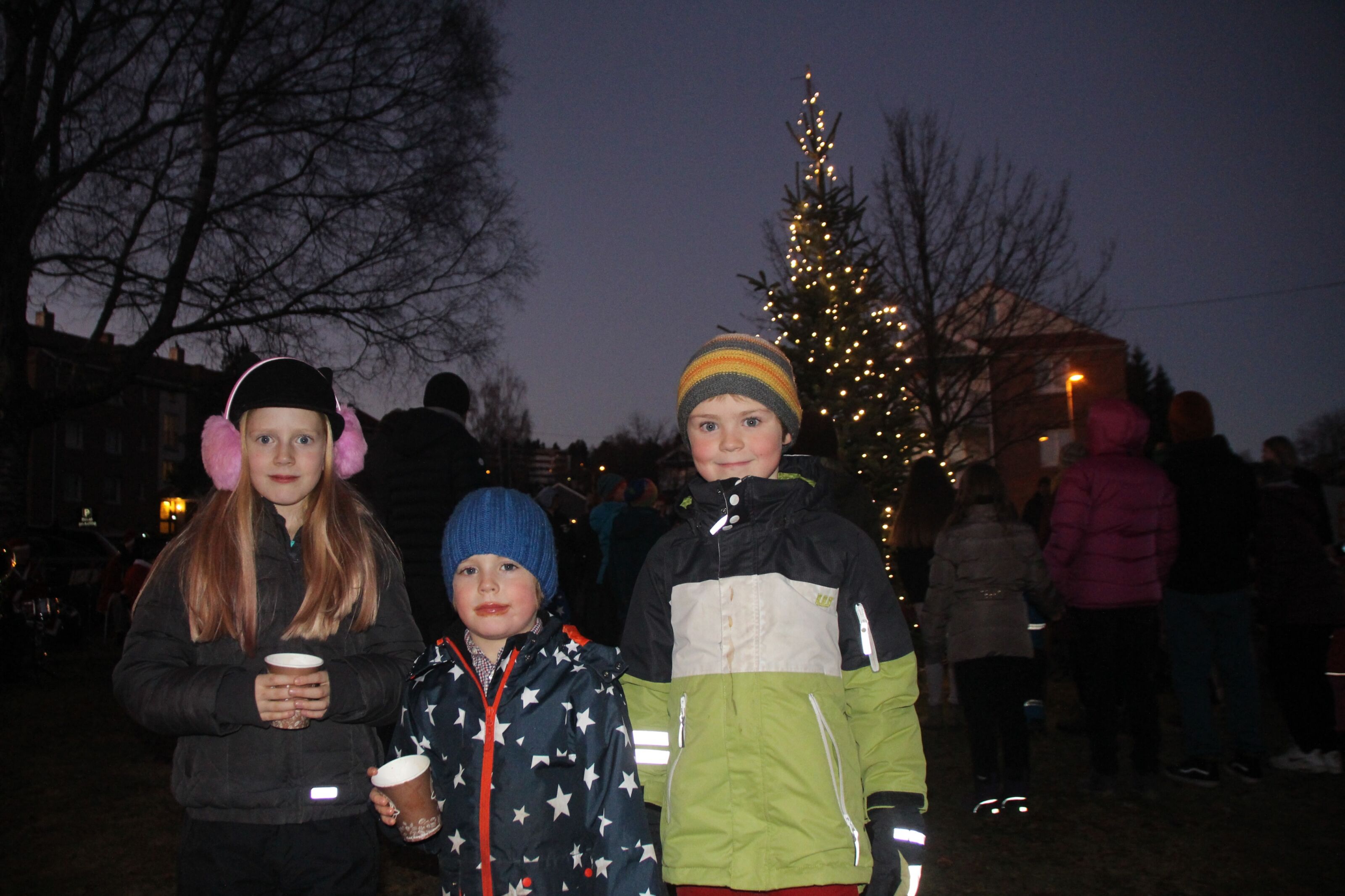 KOSER SEG: Mia (8), Liam (4) og Kasper (7) varmet seg med gløgg mens de så på resten av beboerne i borettslagene danse rundt treet. Foto: