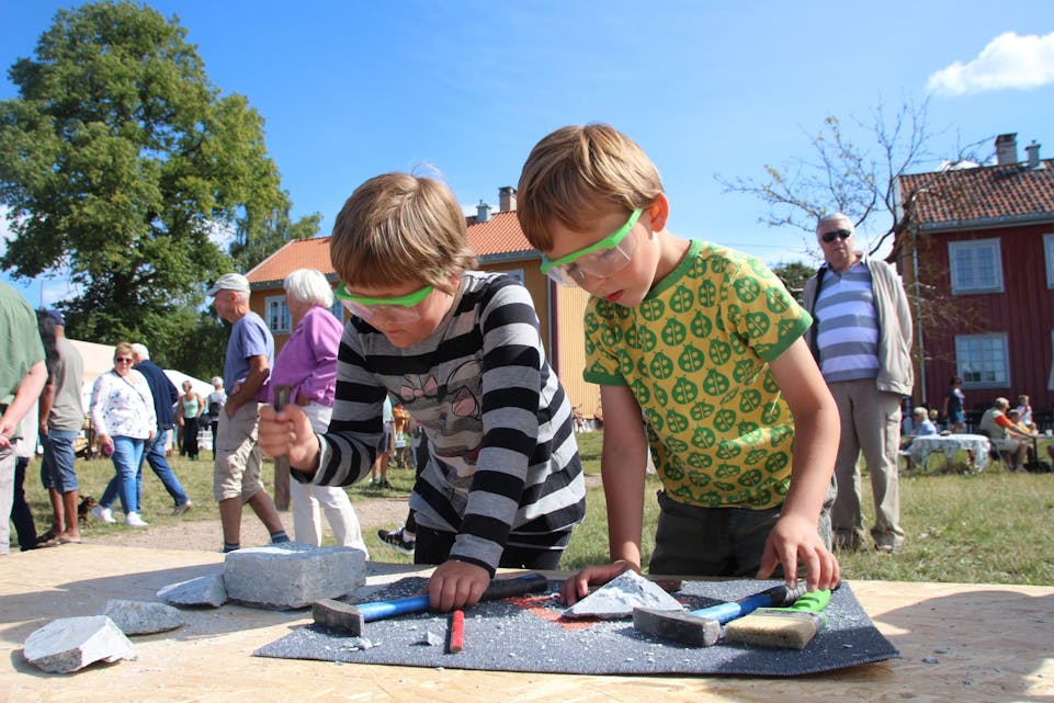 FOR BARNA: I tillegg til muligheter for å hogge i stein, kan barn og unge også delta på steinhoggerkurs i år. Her ser man to gutter som prøver seg med ekte steinhoggerverktøy på festivalen i fjor. Foto:
