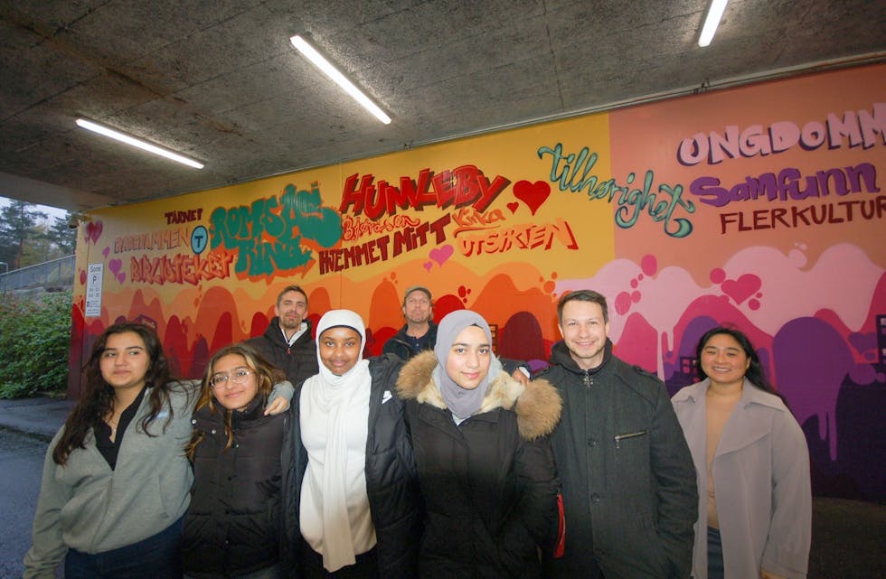 ROMSÅSKUNST: Her står et lite knippe av kunstnerne. Fra venstre: Zahra, Viktoria, Muna og Danja (alle 15). Deretter prosjektleder Tomasz Frelek og Pia Wirum. Bak står Romsås-gatekunstnerne «Dekor-tron» og «Jameone». Foto: