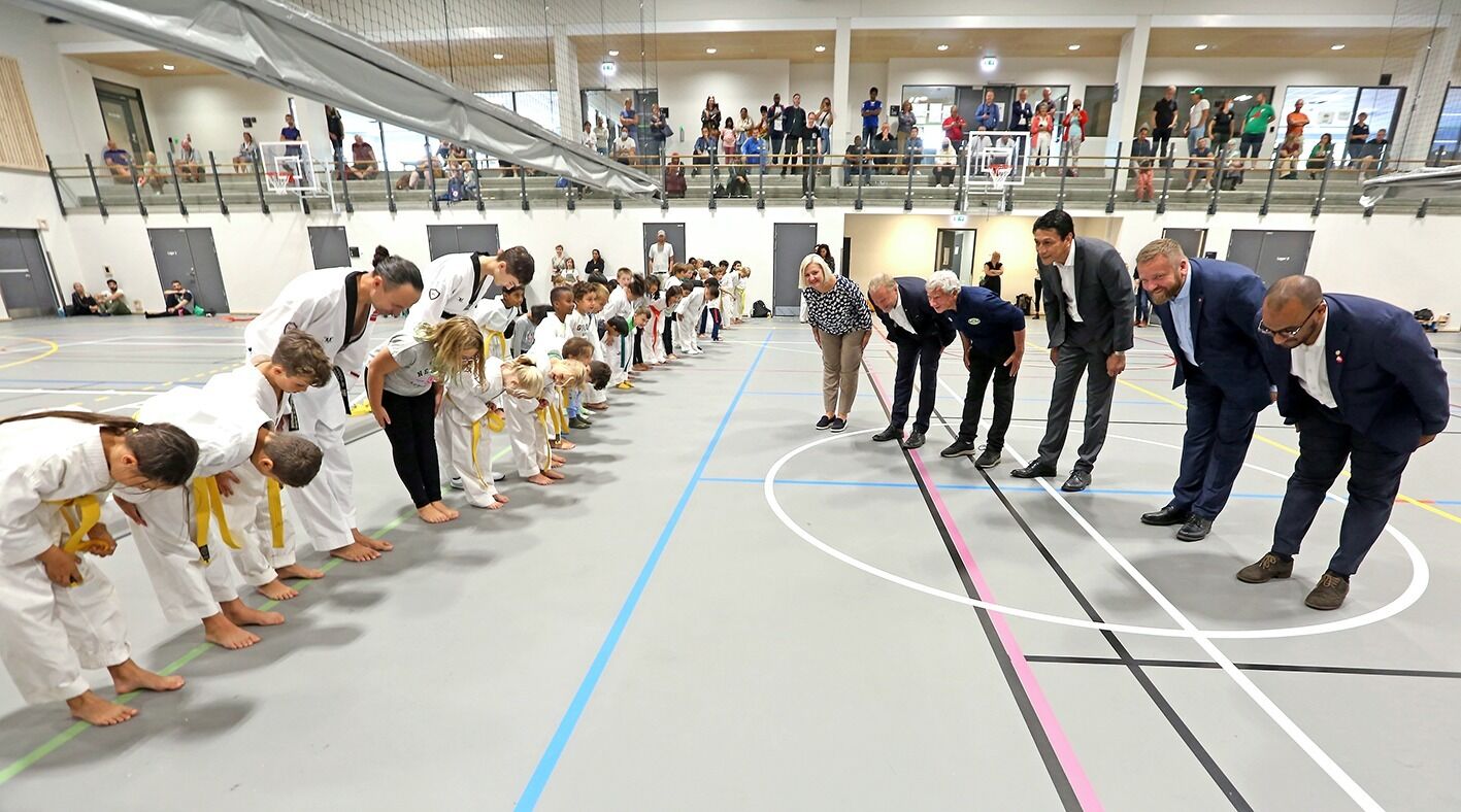 TRADISJONELL HILSEN: Administrerende direktør i Oslobygg KF, Eli Grimsby (f v), byrådsleder Raymond Johansen, leder i Grorud IL, Richard Pedersen, bydelsdirektør Ayub Tughra og BU-leder Anders Røberg-Larsen i Bydel Grorud, samt idrettsbyråd Omar Samy Gamal, utførte tradisjonell hilsen overfor utøverne i Grorud Taekwondo Klubb og deres trener Mikael Oguz (fire f.v. i taekwondo-rekka). Foto: