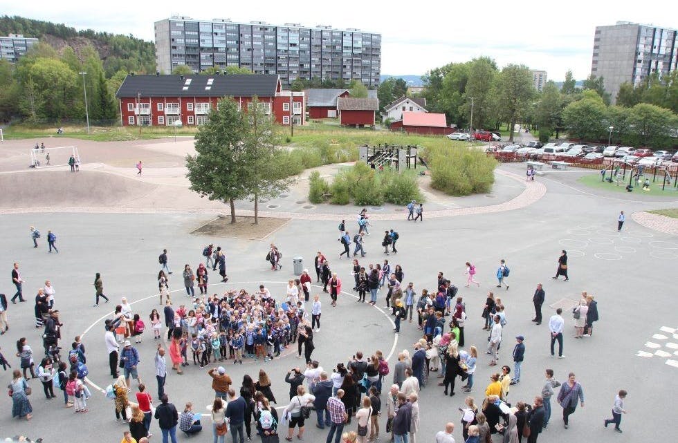 ALLE FØRSTEKLASSINGENE: Etter at første skoledag var over samlet alle førsteklassingene seg i skolegården og vinket til fotografen - som befant seg på verandaen i tredje etasje. Ikke rart at det myldret av folk rundt førsteklassingene, for foreldrene ville sikre seg et bilde av hele gjengen samlet. Foto: