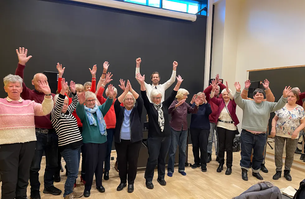 HOPPENDE GLAD: Rustne Røster sangkor har nettopp gjort seg ferdig med øving. Her står de sammen etter å ha sunget sin siste sang for dagen. Mannen i midten med hvit skjorte er den nye dirigenten Jørgen Magnus Haslum.