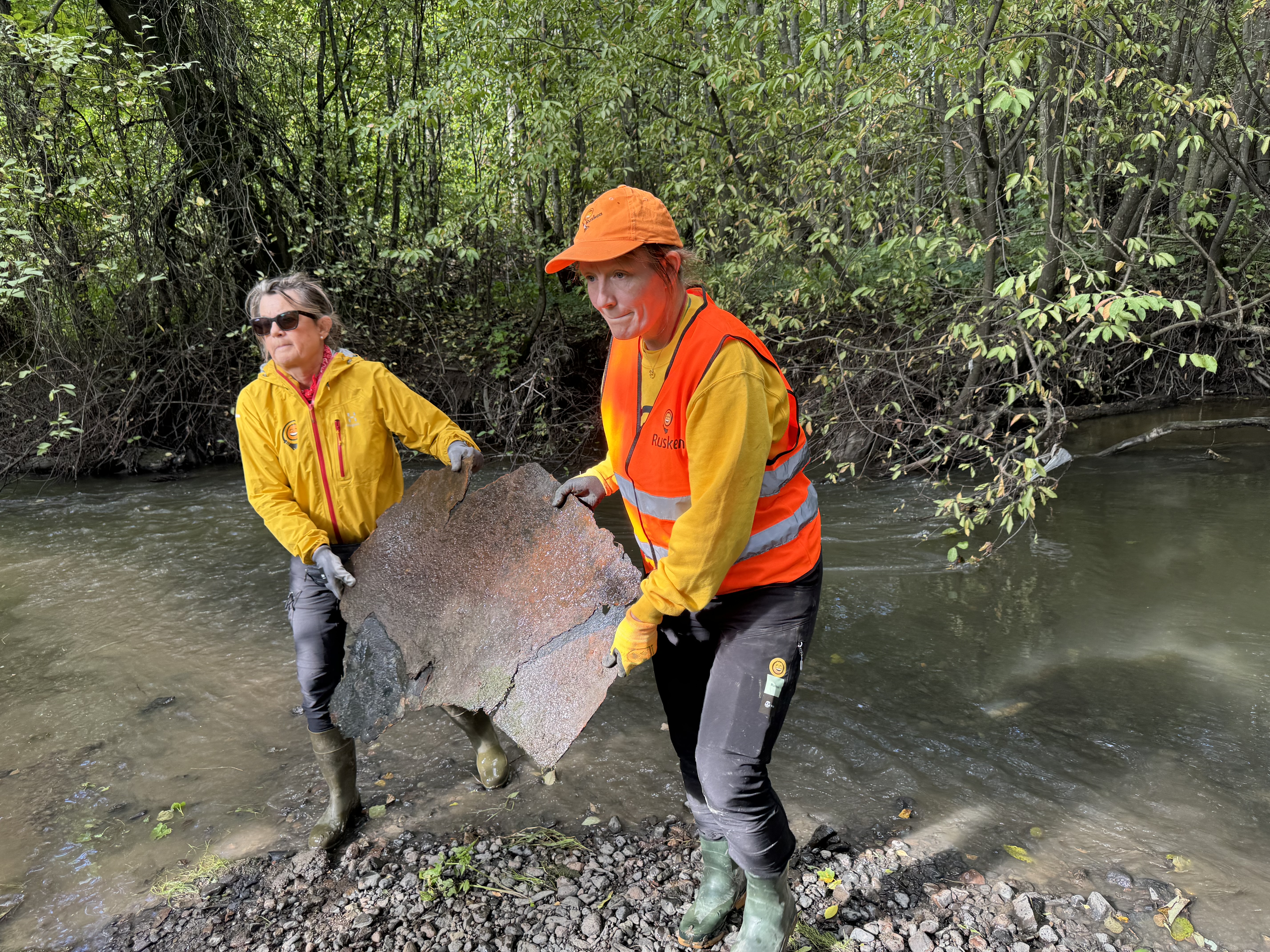 TRIST SYN: Ruskengeneral Jenny Wallheden Krohn og prosjektleder Caroline Magnus bærer en svær metallplate ut av elva.