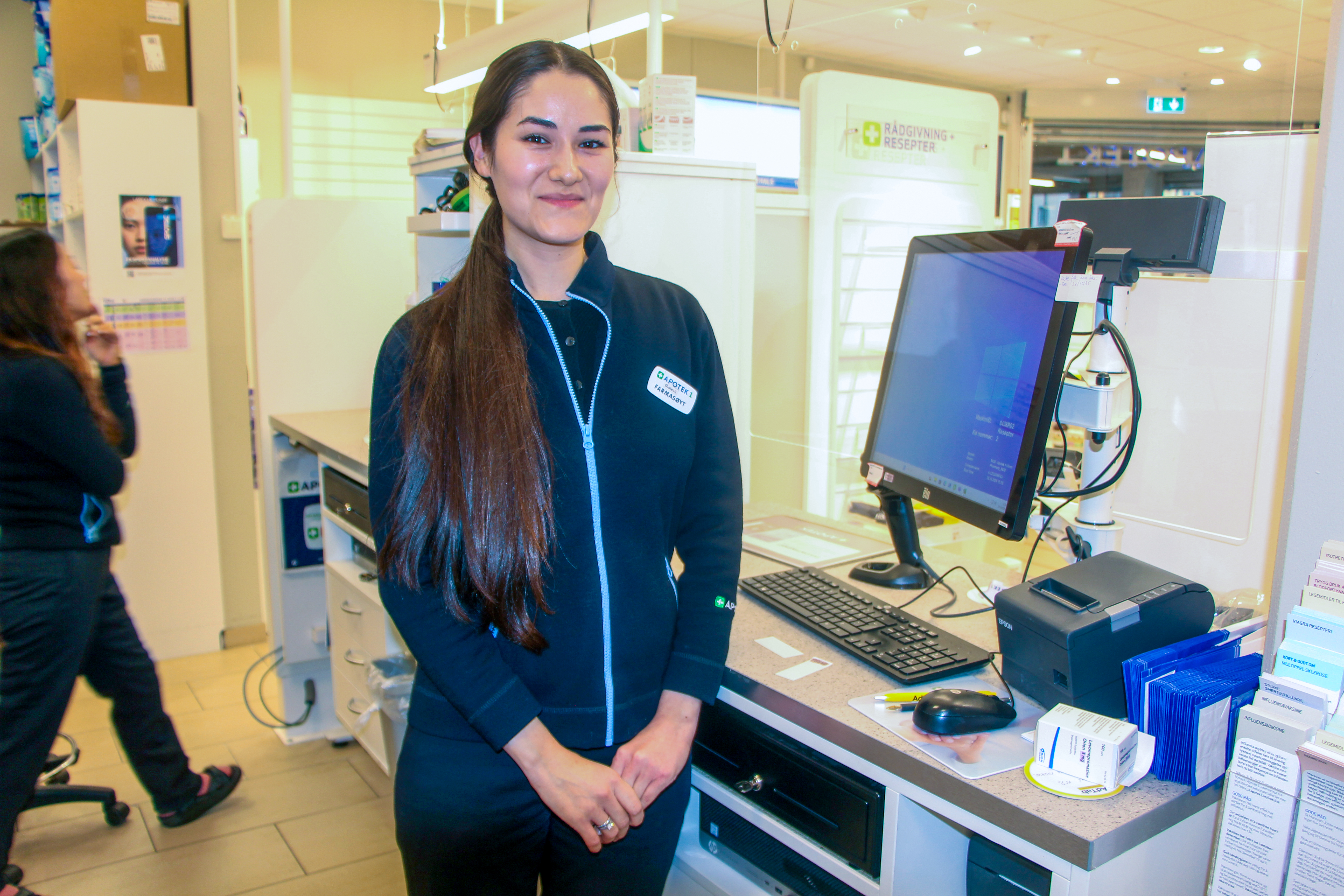 HARDT ARBEID LØNNER SEG: Gunesh Avliiakulova smiler bak disken på Apotek 1 Ulven. Etter fire år i Norge har hun fått bruke utdanningen sin og etablert et nytt liv i trygghet.