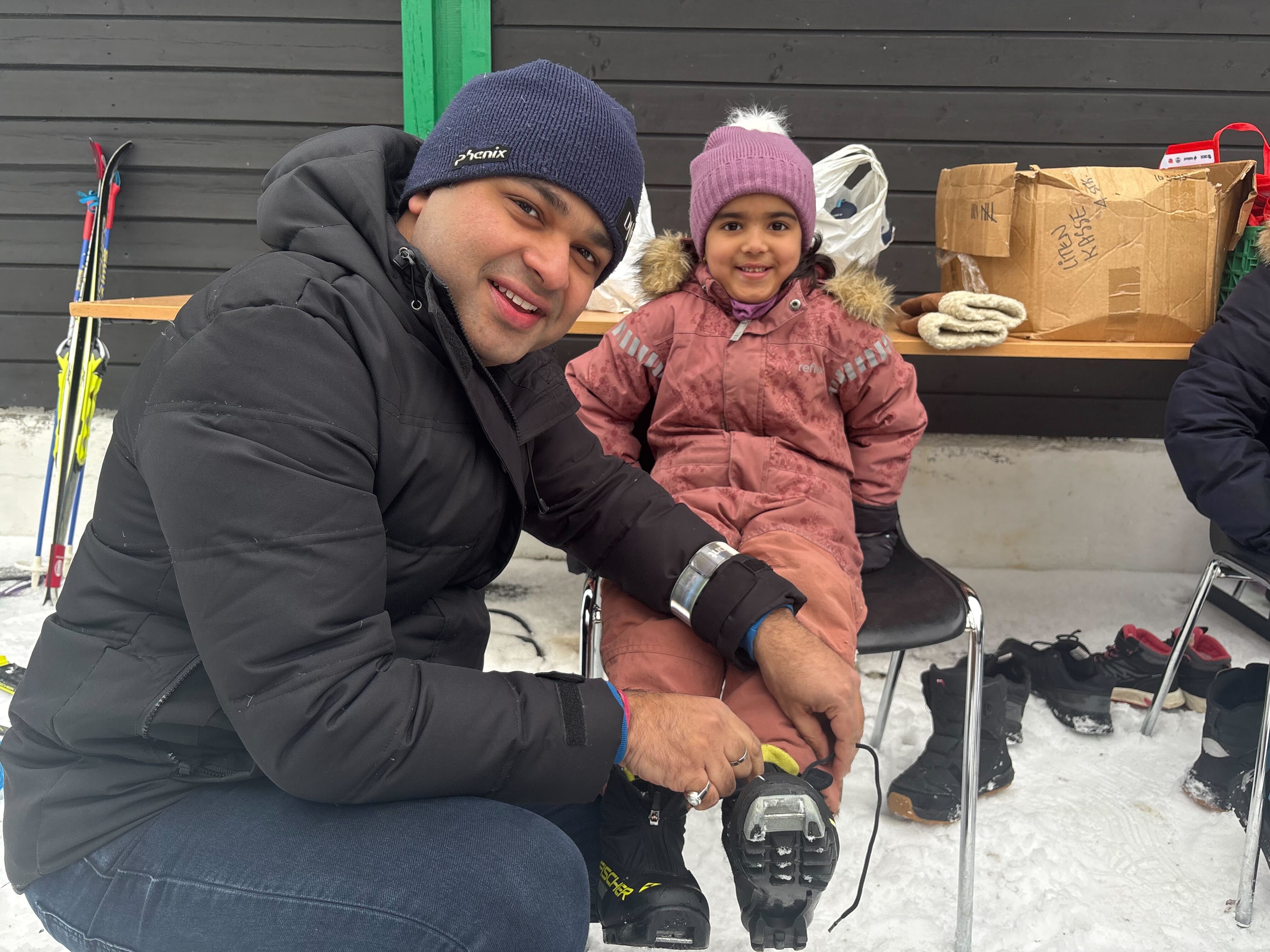 Far hjelper Annika med å få på seg skiskoene de fikk låne av arrangørene.