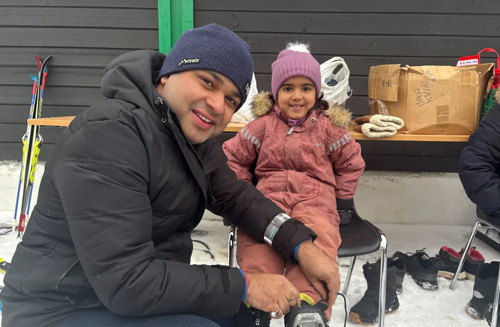 Far hjelper Annika med å få på seg skiskoene de fikk låne av arrangørene.