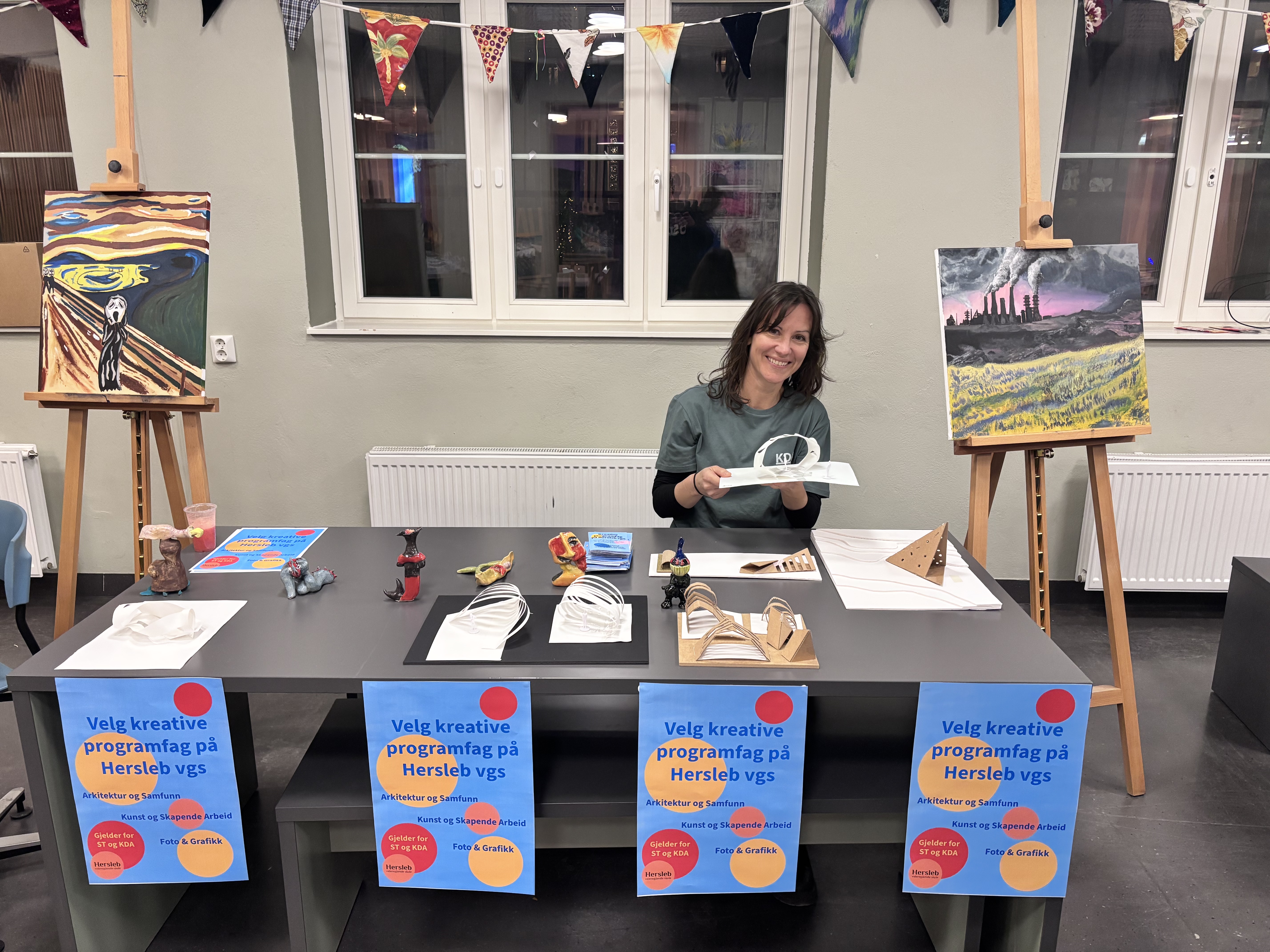 STOLT LÆRER: Nadine Holzheimer sitter komfortabelt i stolen foran utstillingen av de forskjellige kunstverkene laget av hennes elever.