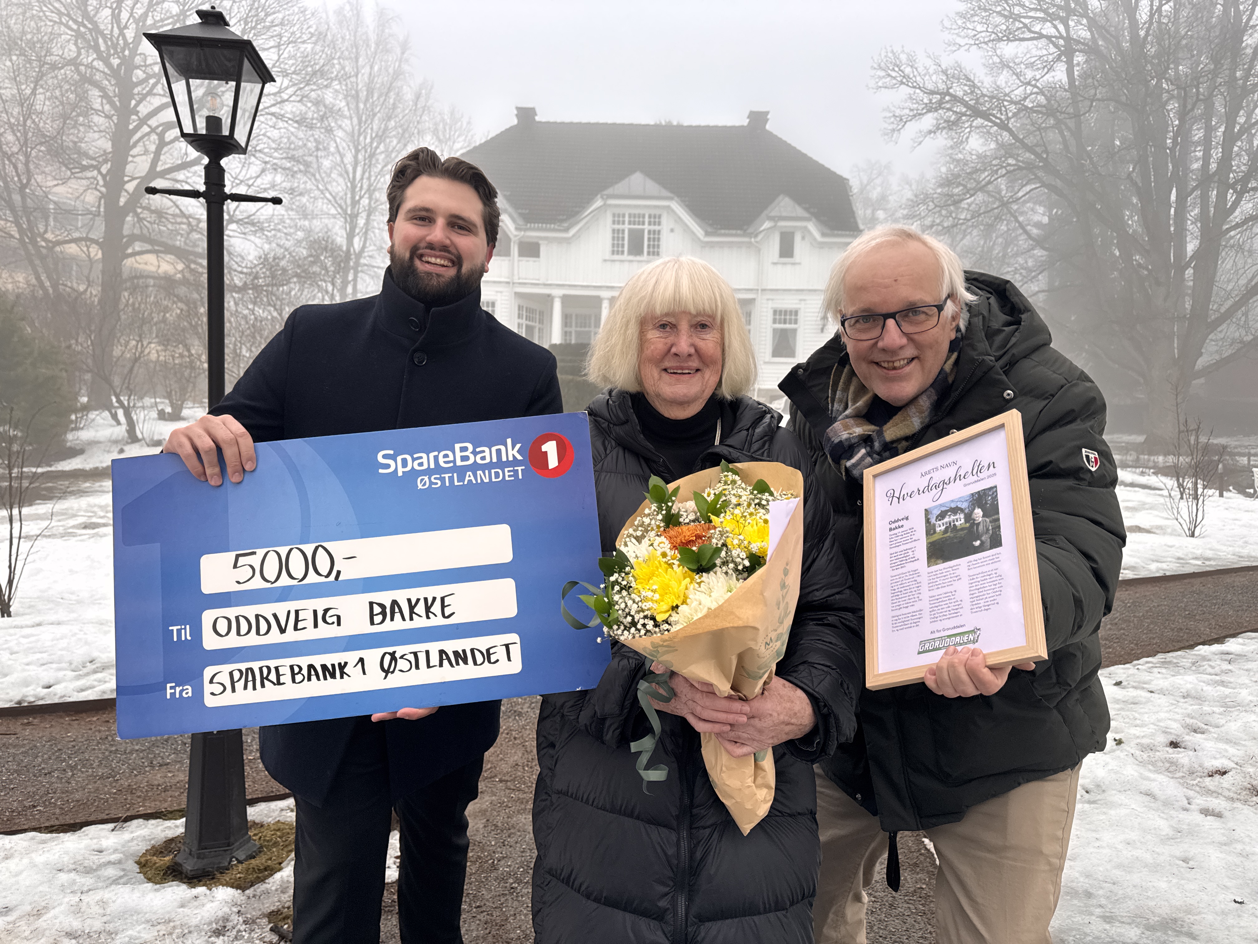 HEDRET I HAGEN: Oddveig Bakke (midten) mottok prisen som Groruddalens hverdagshelt 2025 utenfor Trosterudvillaen. Ruben Gines fra SpareBank 1 Østlandet (t.v.) og Hjalmar jr. Kielland fra Akers Avis Groruddalen (t.h.) sto for overraskelsen.