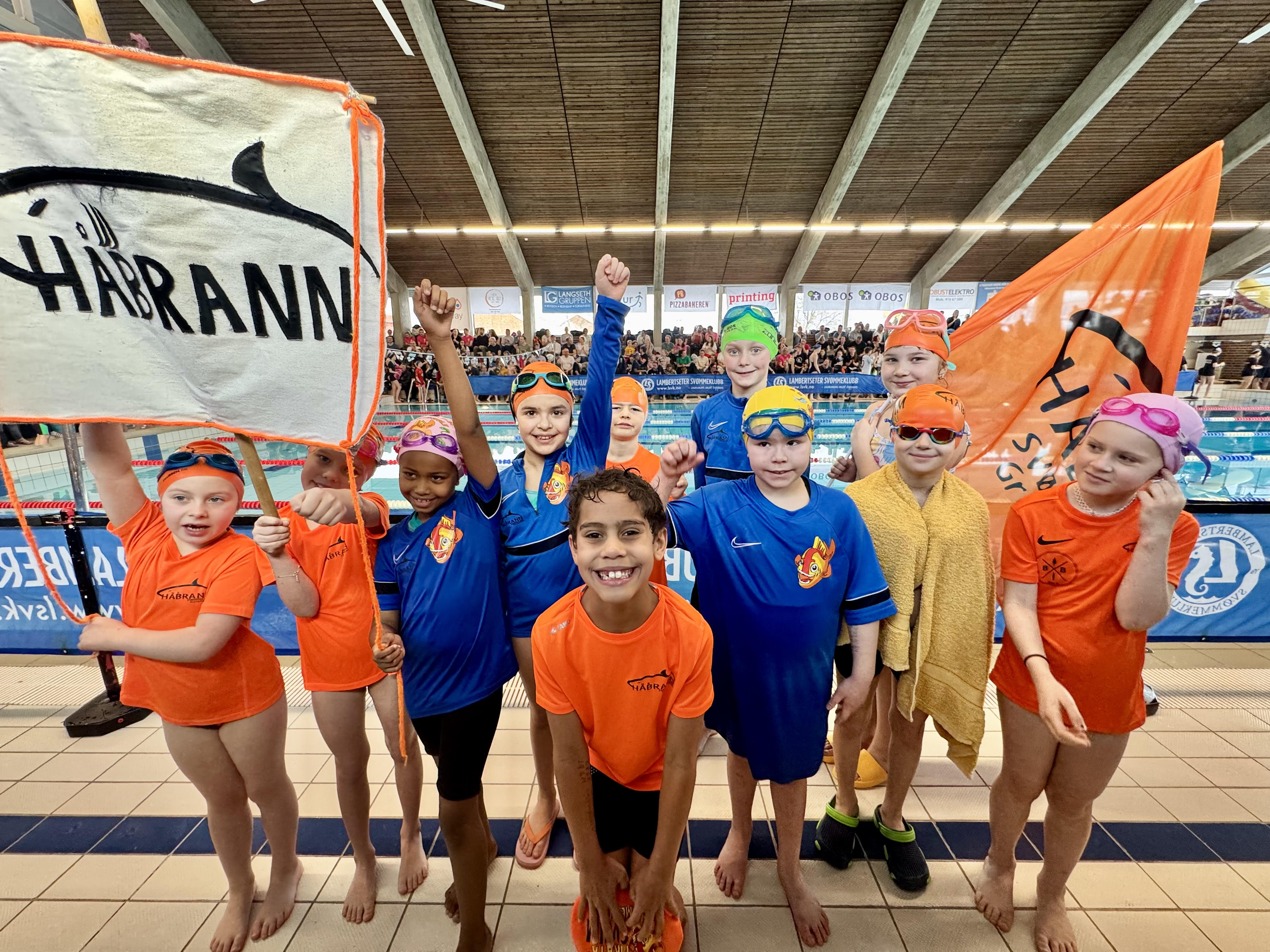 SVØMMEGLEDE I HÅBRANN: Barn fra Håbrann svømmeklubb under stevne med klubbens flagg og farger. Klubben samler barn og unge fra hele nærområdet – og mange ulike nasjonaliteter. (Foto: Lise Martine Halle)