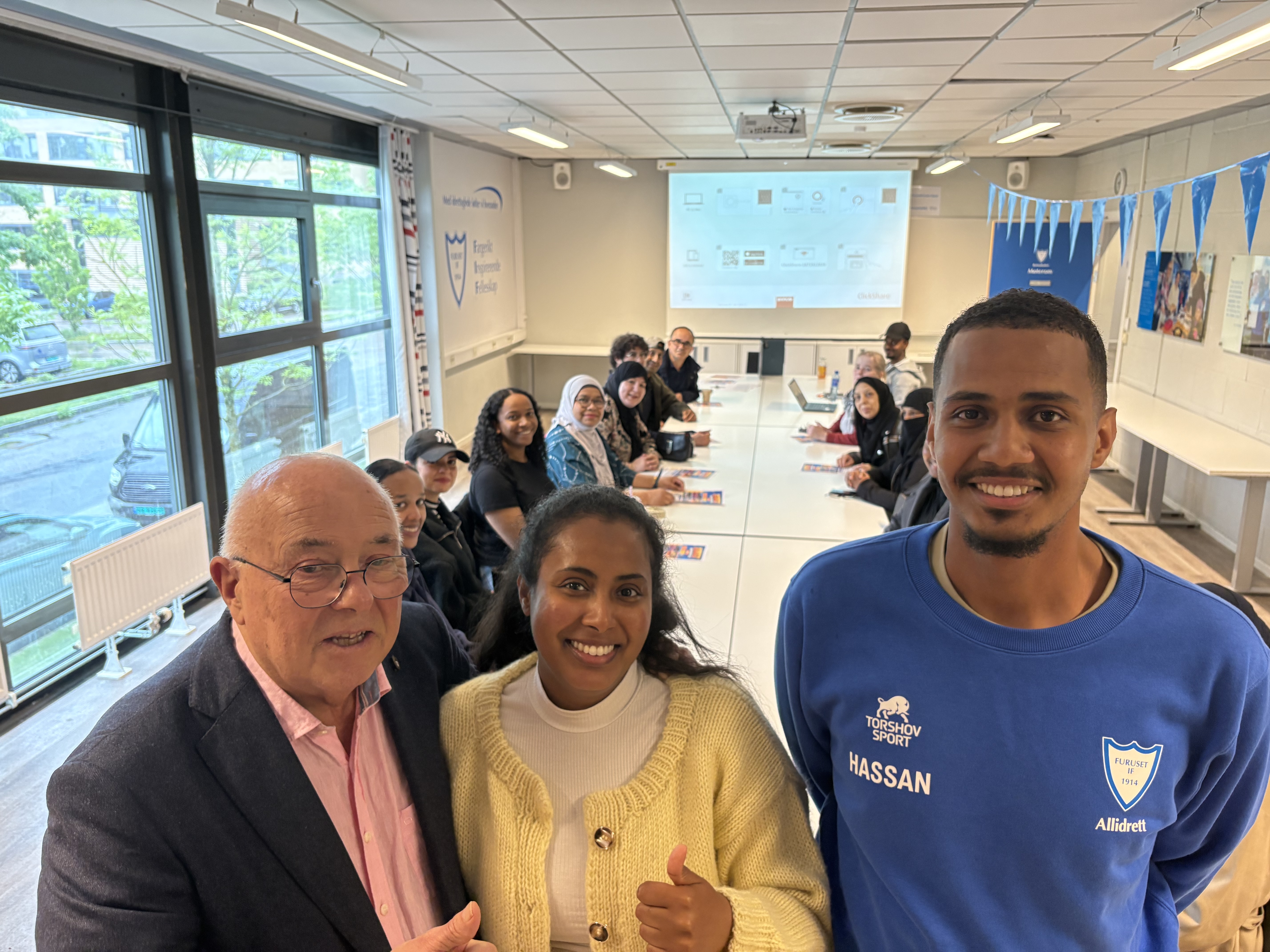 SAMMEN FOR FURUSET: Vidar Noreng (t.v.) fra Furuset Vel og Furuset IF, frivillighetskoordinator Yusra Hasan i FUBIAK og Hassan Salah Hassan, leder for Alnaskolen for unge ledere i Furuset IF, gleder seg til Furusets Nabolagsfestival. I bakgrunnen er frivillige og samarbeidspartnere samlet under planleggingen av årets festival.