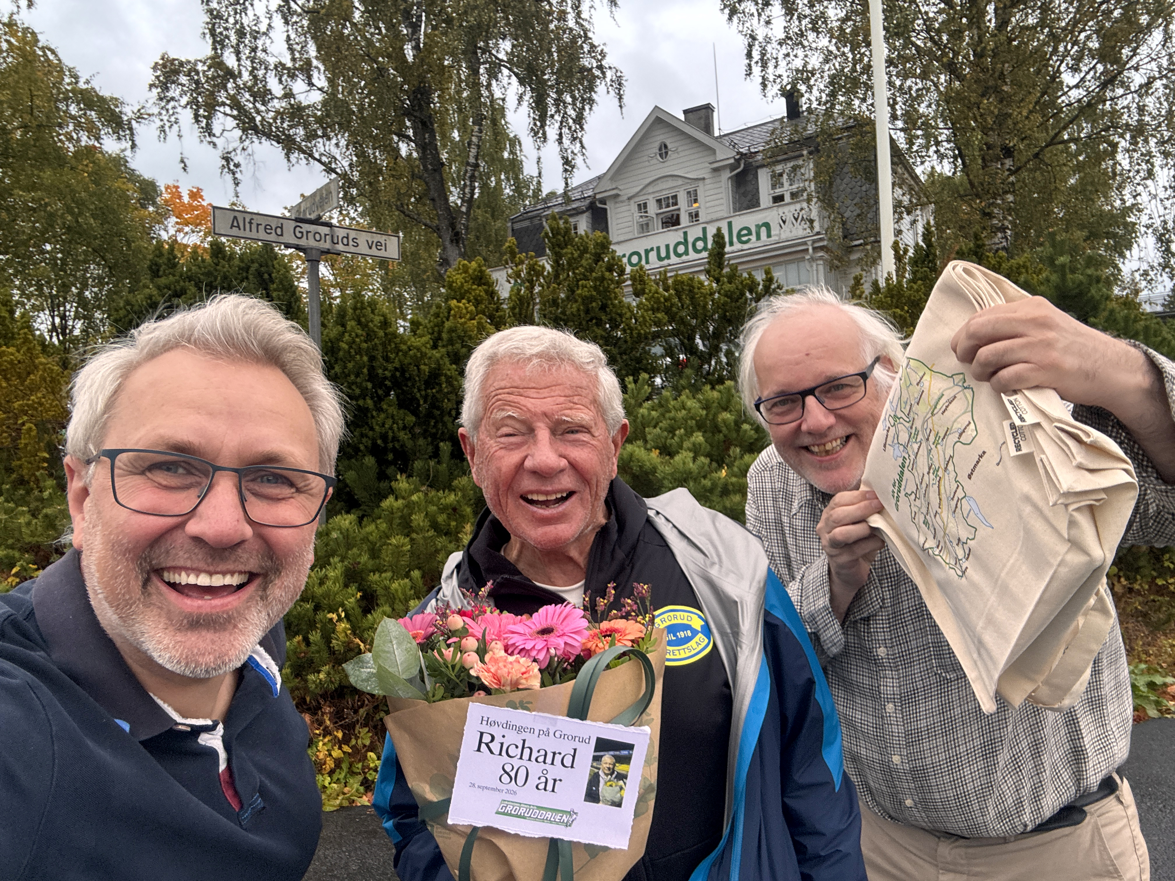 INVITERT TIL AVISHUSET... Høvdingen på Grorud ble invitert til avishuset mandag 28. september 2026. Vi heiste flagget for Richard Pedersen som runder 80 år denne dag. Han var akkurat kommet hjem fra en to og en halv timers «rask gange» i Lillomarka, noe han gjør fem dager i uka. De to siste dagene går han i normalt tempo som oss andre. Det blir altså syv dager i uka for den spreke fotballnestoren her på Grorud. Vi gratulerer med den store dagen! Lokalavisens to av tre brødre, Øystein (t.v.) og Hjalmar jr., benyttet også anledningen til en selfie foran flaggstang og avishus.